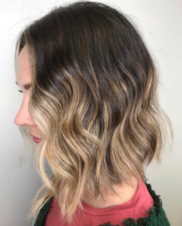 Dark roots melting into blonde balayage on a wavy lob, side view