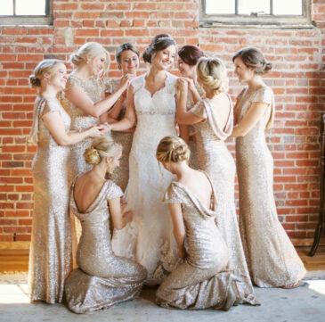 Bridesmaids in champagne sequin gowns with updos gathered around the bride