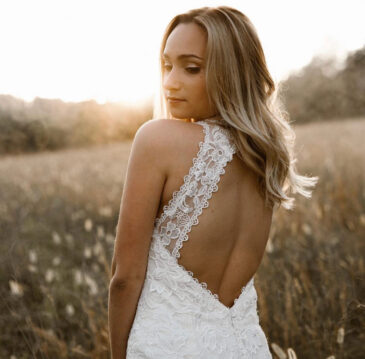 Bride with long soft blonde waves in a lace open-back gown in a sunlit field