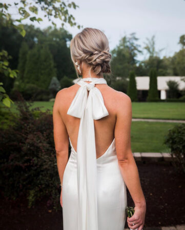 Back view of a bride with a braided low bun and an open-back halter gown tied with a bow