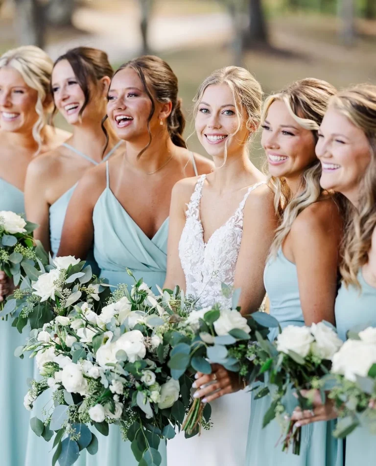Smiling bride and bridesmaids in dusty blue dresses with soft curled wedding hair