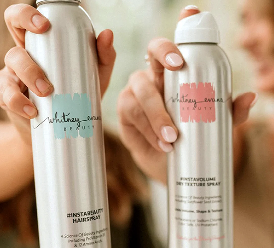Hands holding Whitney Evans Beauty InstaBeauty Hairspray and InstaVolume Dry Texture Spray